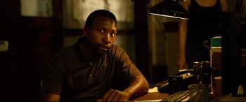 Movie still from “Spiral” (2021), directed by Darren Lynn Bousman – A man sitting at a table in front of a lamp; Close Up shot, Low angle