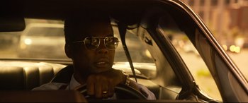Movie still from “Spiral” (2021), directed by Darren Lynn Bousman – A man driving in a car wearing sunglasses; Close Up shot, Low angle