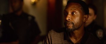 Movie still from “Spiral” (2021), directed by Darren Lynn Bousman – A person sitting in a room; Close Up shot, Over the shoulder angle