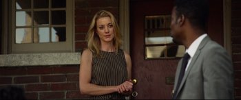 Movie still from “Spiral” (2021), directed by Darren Lynn Bousman – A beautiful blonde woman holding a knife in front of a brick building; Medium shot, Over the shoulder angle