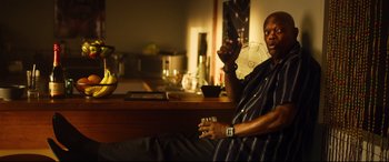 Movie still from “Spiral” (2021), directed by Darren Lynn Bousman – A man sitting in front of a counter holding a remote control; Medium shot, Low angle