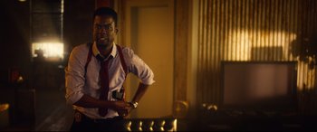 Movie still from “Spiral” (2021), directed by Darren Lynn Bousman – A man in a white shirt and red tie holding a cell phone; Medium shot, Over the shoulder angle