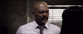 Movie still from “Spiral” (2021), directed by Darren Lynn Bousman – A bald man with a mustache and a purple tie; Close Up shot, Low angle