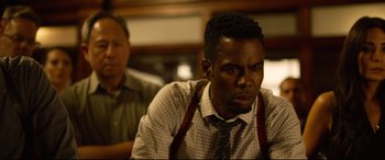Movie still from “Spiral” (2021), directed by Darren Lynn Bousman – A man in a tie sitting at a table with another man; Close Up shot, Over the shoulder angle