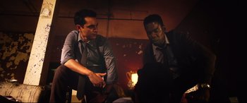Movie still from “Spiral” (2021), directed by Darren Lynn Bousman – Two men in business suits sitting next to each other in a dimly - lit room; Medium shot, Low angle