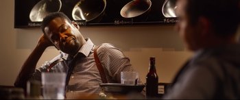 Movie still from “Spiral” (2021), directed by Darren Lynn Bousman – A man sitting at a table with a beer in front of him; Close Up shot, Low angle