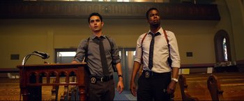 Movie still from “Spiral” (2021), directed by Darren Lynn Bousman – A couple of men standing next to each other in a room; Medium shot, Low angle