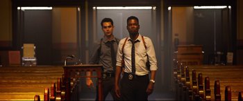 Movie still from “Spiral” (2021), directed by Darren Lynn Bousman – A couple of men standing next to each other in a room; Medium shot, Low angle