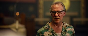 Movie still from “Spiral” (2021), directed by Darren Lynn Bousman – An older man wearing glasses and a hawaiian shirt; Close Up shot, Low angle