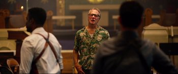 Movie still from “Spiral” (2021), directed by Darren Lynn Bousman – A man wearing a hawaiian shirt standing in front of a crowd; Medium shot, Over the shoulder angle