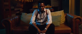 Movie still from “Spiral” (2021), directed by Darren Lynn Bousman – A man sitting on a couch in a living room; Medium shot, High angle