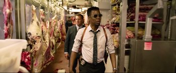 Movie still from “Spiral” (2021), directed by Darren Lynn Bousman – A man in sunglasses and a tie walking down a hallway; Medium shot, Over the shoulder angle