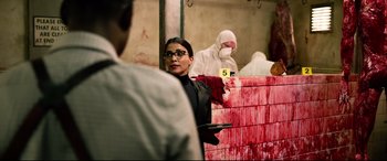 Movie still from “Spiral” (2021), directed by Darren Lynn Bousman – A woman in black shirt holding a pair of scissors in a room; Medium shot, Over the shoulder angle