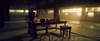 Movie still from “Spiral” (2021), directed by Darren Lynn Bousman – A man sitting at a wooden table in a room; Wide shot, Low angle