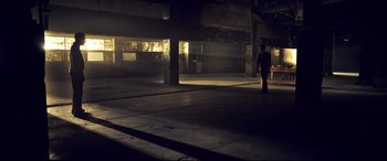 Movie still from “Spiral” (2021), directed by Darren Lynn Bousman – A person standing in a dark room with a light shining on them; Extreme Wide shot, Low angle