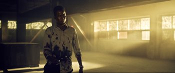 Movie still from “Spiral” (2021), directed by Darren Lynn Bousman – A young man holding a skate board in a room; Medium shot, Low angle