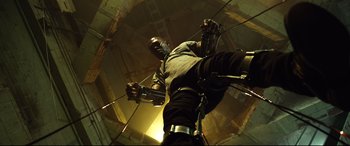 Movie still from “Spiral” (2021), directed by Darren Lynn Bousman – A man is hanging on a rope in a building; Wide shot, Low angle