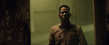 Movie still from “Spiral” (2021), directed by Darren Lynn Bousman – A man with blood on his shirt is standing in a dark room; Close Up shot, Low angle