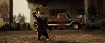 Movie still from “Spiral” (2021), directed by Darren Lynn Bousman – A pig marionette in front of a truck; Wide shot, Low angle