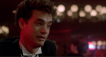 Movie still from “Splash” (1983), directed by Ron Howard – A man in a suit and tie sitting in front of a crowd; Close Up shot, Over the shoulder angle