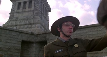 Movie still from “Splash” (1983), directed by Ron Howard – A man in a military uniform standing in front of a stone building; Medium shot, Low angle