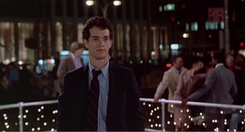 Movie still from “Splash” (1983), directed by Ron Howard – A man in a suit and tie standing in front of a crowd; Medium shot, Over the shoulder angle