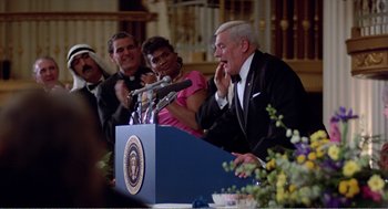 Movie still from “Splash” (1983), directed by Ron Howard – A man in a suit is speaking at a podium; Medium shot, Over the shoulder angle