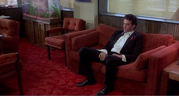 Movie still from “Splash” (1983), directed by Ron Howard – A man sitting on a red couch in a room; Wide shot, High angle