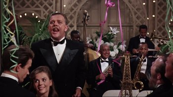 Movie still from “Splendor in the Grass” (1961), directed by Elia Kazan – A group of people in tuxedos singing in front of an eiffel tower; Medium shot, Over the shoulder angle