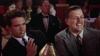 Movie still from “Splendor in the Grass” (1961), directed by Elia Kazan – Two men in suits sitting at a table in front of a crowd; Medium shot, Over the shoulder angle