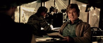 Movie still from “Spy Game” (2001), directed by Tony Scott – A man sitting at a table in a room; Medium shot, Over the shoulder angle