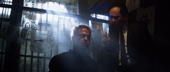 Movie still from “Spy Game” (2001), directed by Tony Scott – A man is smoking a cigarette while another man looks on; Medium shot, Low angle