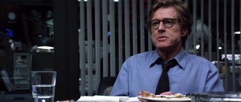 Movie still from “Spy Game” (2001), directed by Tony Scott – A man sitting at a table eating a piece of pizza; Close Up shot, Over the shoulder angle