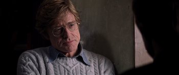 Movie still from “Spy Game” (2001), directed by Tony Scott – An older man wearing glasses and a sweater looks at the camera; Close Up shot, Over the shoulder angle