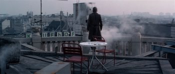 Movie still from “Spy Game” (2001), directed by Tony Scott – A man standing on top of a building next to a table; Wide shot, Low angle