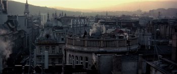 Movie still from “Spy Game” (2001), directed by Tony Scott – A man standing on top of a building near a city; Extreme Wide shot, Low angle