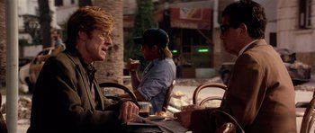 Movie still from “Spy Game” (2001), directed by Tony Scott – A group of people sitting at a table with food; Medium shot, Over the shoulder angle