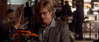 Movie still from “Spy Game” (2001), directed by Tony Scott – A person sitting at a table with a vase of flowers; Close Up shot, Over the shoulder angle