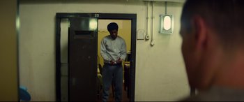 Movie still from “Starred Up” (2013), directed by David Mackenzie – A man standing in a doorway holding a cell phone; Wide shot, Low angle