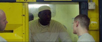 Movie still from “Starred Up” (2013), directed by David Mackenzie – A man wearing a white hat sitting in front of a window; Medium shot, Over the shoulder angle