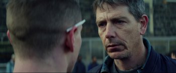 Movie still from “Starred Up” (2013), directed by David Mackenzie – A man is looking at another man with a cigarette in his ear; Close Up shot, Over the shoulder angle