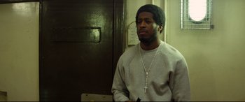 Movie still from “Starred Up” (2013), directed by David Mackenzie – A man with a rosary in a room; Medium shot, Low angle