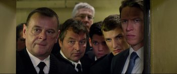 Movie still from “Starred Up” (2013), directed by David Mackenzie – A group of men standing next to each other in suits; Medium shot, High angle