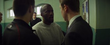 Movie still from “Starred Up” (2013), directed by David Mackenzie – A man in a white shirt is talking to two other men; Medium shot, Over the shoulder angle
