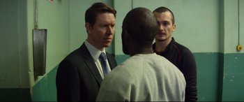 Movie still from “Starred Up” (2013), directed by David Mackenzie – A man in a business suit talking to two other men; Medium shot, Over the shoulder angle