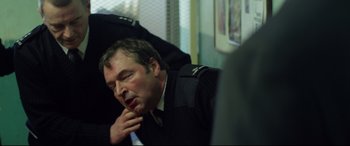 Movie still from “Starred Up” (2013), directed by David Mackenzie – A man in a police uniform sitting in front of a window; Close Up shot, Over the shoulder angle