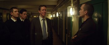 Movie still from “Starred Up” (2013), directed by David Mackenzie – A man wearing a suit and tie in a hallway; Medium shot, Over the shoulder angle