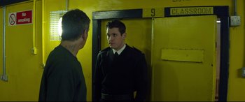 Movie still from “Starred Up” (2013), directed by David Mackenzie – A man standing in front of a door looking at another man; Medium shot, Over the shoulder angle
