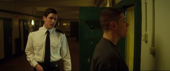 Movie still from “Starred Up” (2013), directed by David Mackenzie – A police officer standing next to a man in front of a green door; Medium shot, Over the shoulder angle