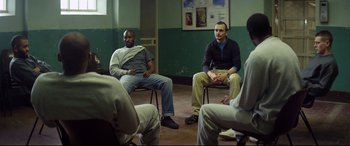 Movie still from “Starred Up” (2013), directed by David Mackenzie – A group of men sitting in a circle in a room; Wide shot, High angle